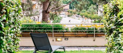 Un balcón con una silla, con vista a una calle llena de flores amarillas y árboles.