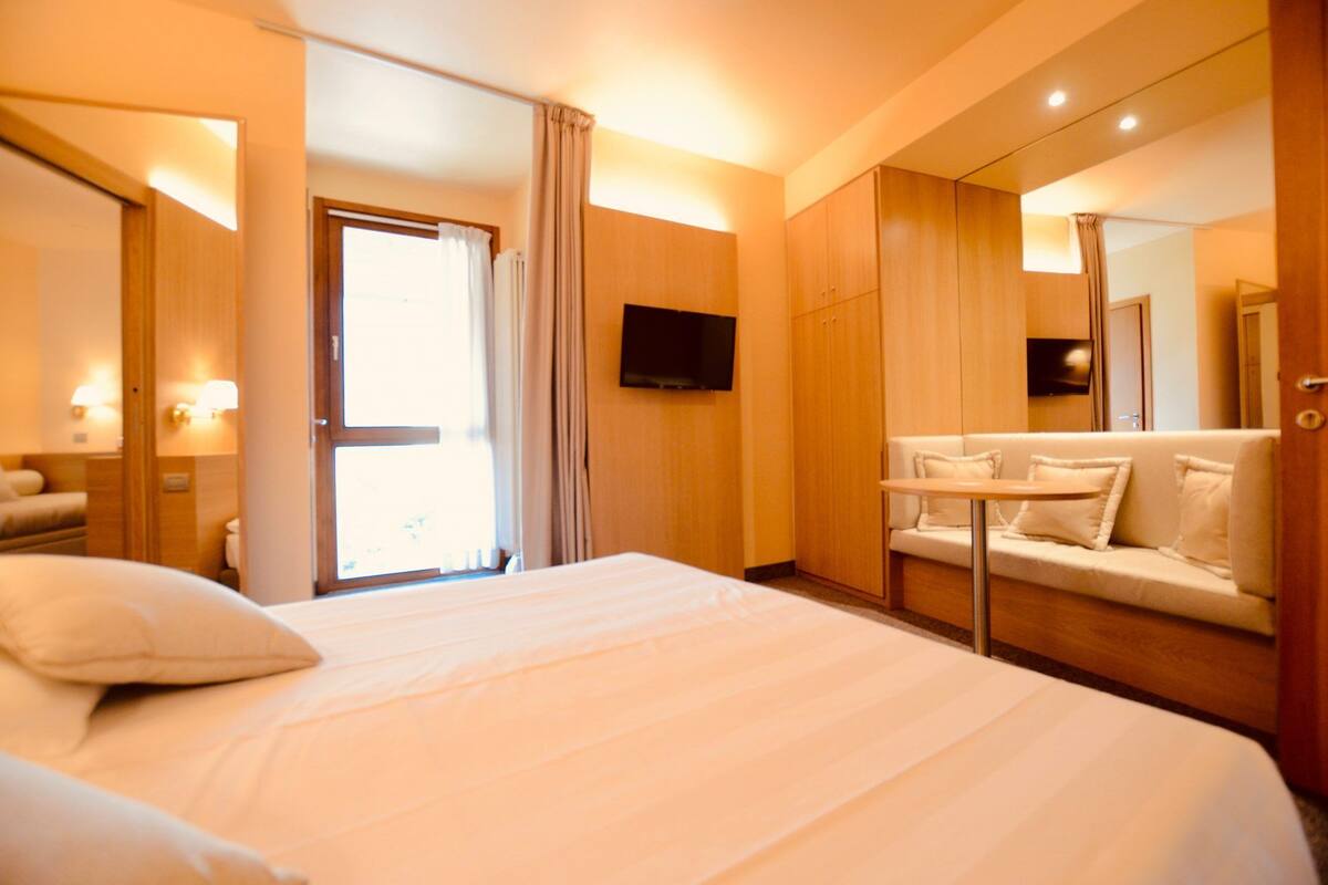 Een hotelkamer met een groot bed, een slaapbank, een aan de muur bevestigde televisie en een spiegel.