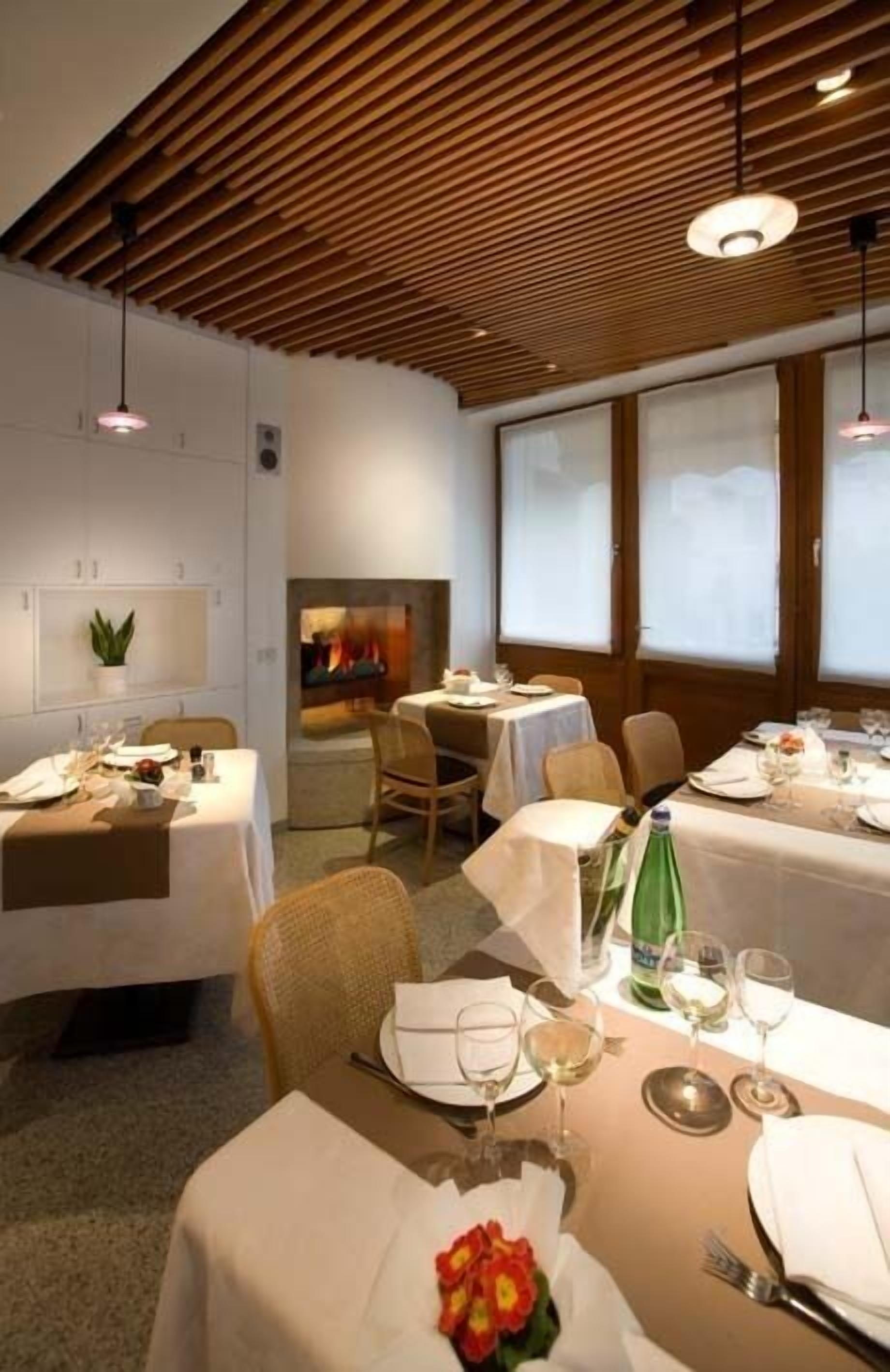 A dining area with tables set for two, a fireplace, and large windows.