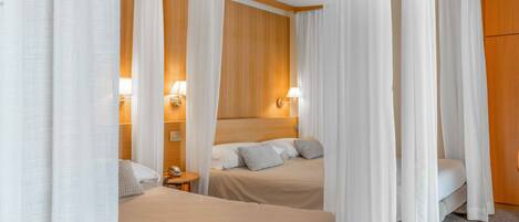 Una habitación de hotel con dos camas, cabeceros de madera, cortinas blancas, lámparas de noche y un armario de madera.