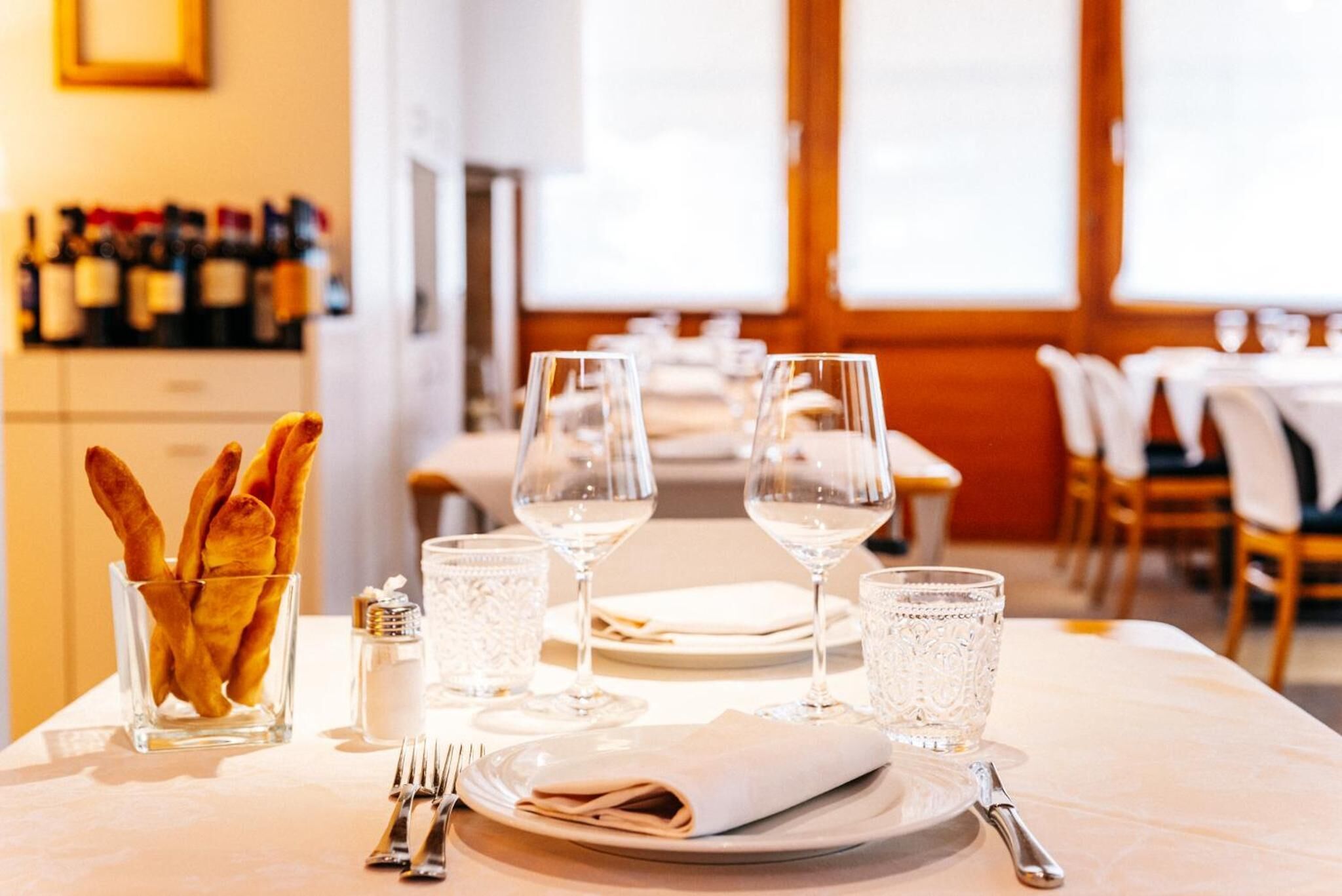 A dining table set with plates, glasses, and cutlery, with a bottle of wine and a glass of water in the background.