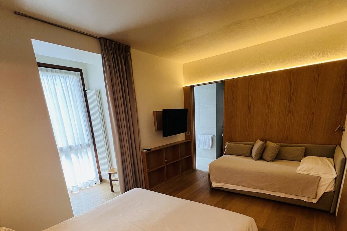 Een hotelkamer met een groot bed, een kleinere bank, een aan de muur bevestigde televisie en een houten paneelwand.