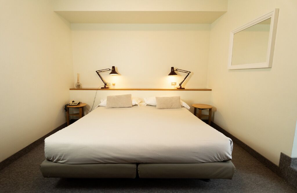 A neatly made bed with a headboard, two bedside tables with lamps, and a small shelf above the bed.