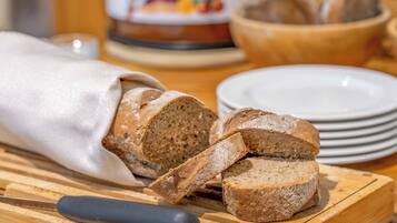 A loaf of bread on a wooden cutting board with a knife, surrounded by plates and a jar of jam.