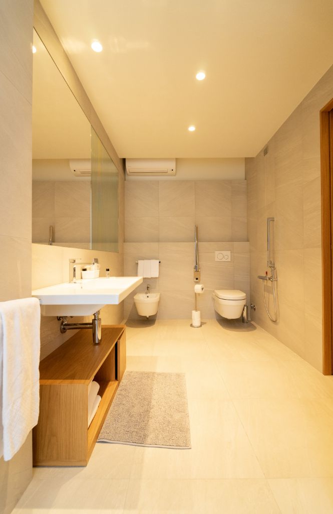 Ein modernes Badezimmer mit großem Spiegel, Waschtisch aus Holz, Toilette und Duschbereich.