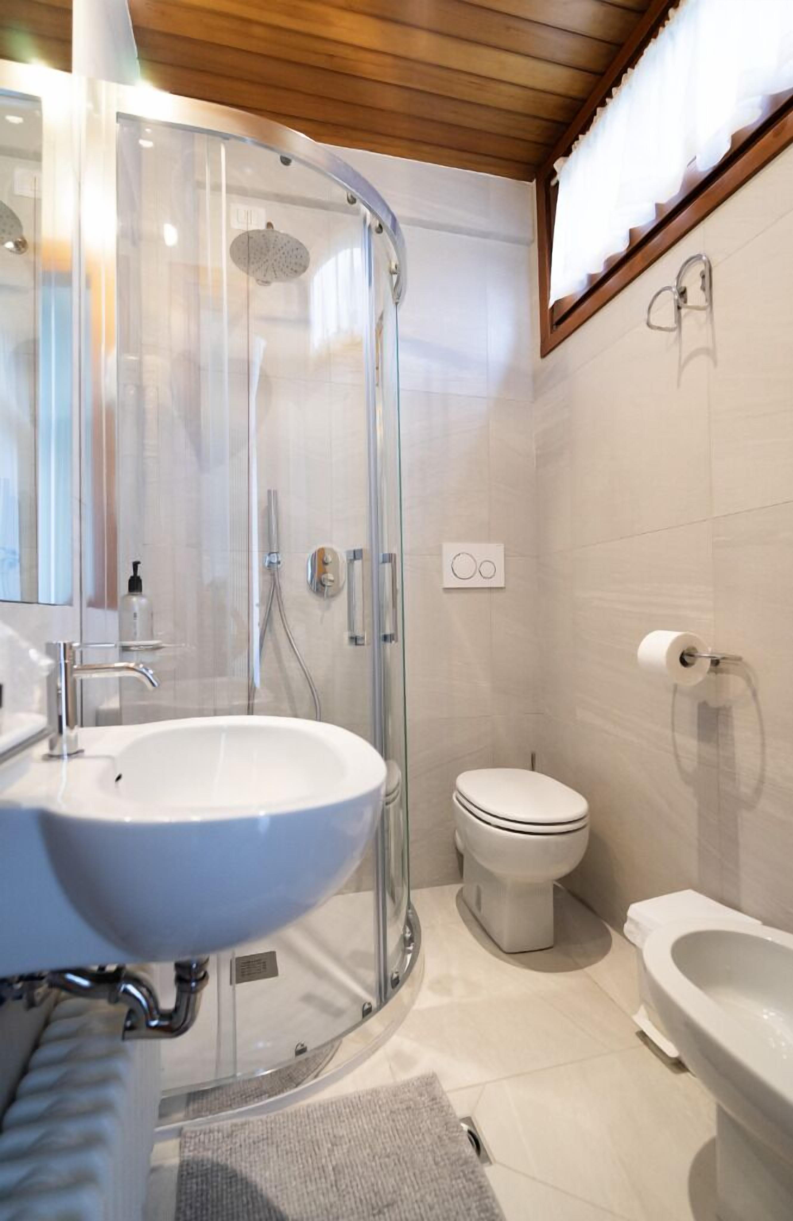 Un baño moderno con ducha envuelta en vidrio, un lavamanos blanco, un inodoro y una bañera.