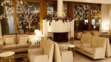 A cozy living room with a fireplace, comfortable sofas, and large windows with festive lights.