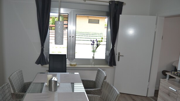 Un coin repas comprenant une table, des chaises, un vase avec des fleurs et une fenêtre avec des rideaux.