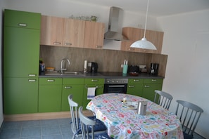Une cuisine avec des armoires vertes, un plan de travail en bois, une cuisinière et une table recouverte d’une nappe colorée.