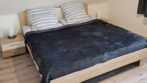 Une chambre à coucher avec un lit en bois, deux oreillers, une table de chevet avec une lampe et une fenêtre avec des rideaux.