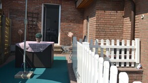 Un bâtiment en briques avec une clôture blanche en bois, un patio couvert avec une table et des chaises, et une porte donnant sur un espace intérieur.