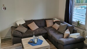 Un salon moderne avec un canapé d’angle, une table basse en bois et un petit tabouret.