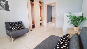 A living room with a grey sofa, a black and white polka dot pillow, a wooden cabinet, and a potted plant. - Chloe Apartments (Kefalonia)