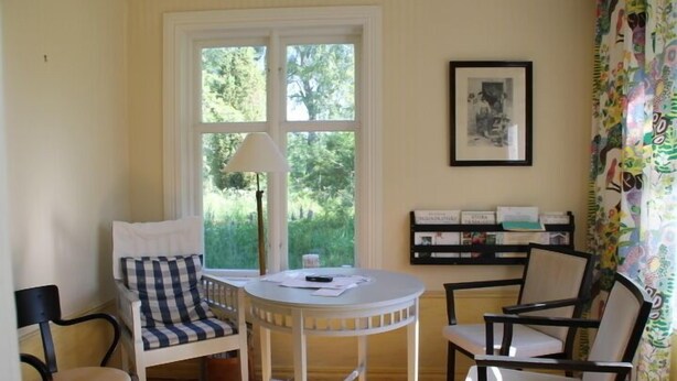 A room with a round table, two chairs, a lamp, and a bookshelf with books. - Holiday home Törnamåla Kilen (Tingsryd)