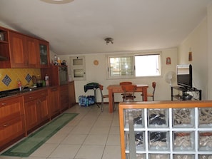 A kitchen with wooden cabinets, a dining table with chairs, a TV, and a window with blinds.