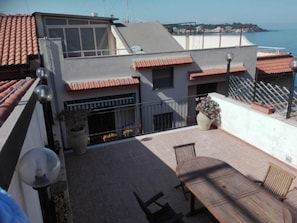 A rooftop terrace with a table and chairs, a potted plant, and a view of the sea.