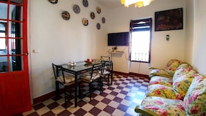 A dining area with a checkered floor, a glass table, and four chairs. There is a sofa with a floral pattern and a television mounted on the wall. - Fantastic Penthouse in Plaza Elvira next to the Cathedral  (Sevilla)