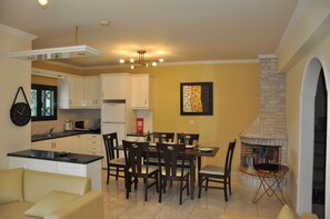 A modern kitchen with white cabinets, a dining area with a table and chairs, and a fireplace.