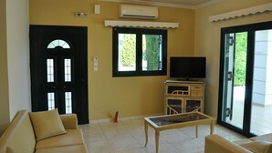 Una sala de estar con sofá, mesa de centro, televisor y puerta corrediza de vidrio que da a un balcón.