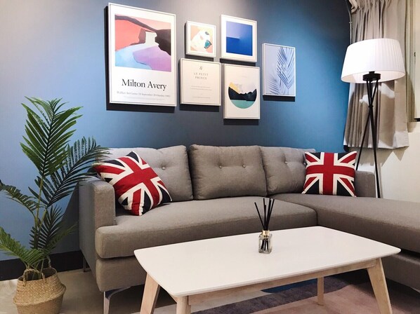 A living room with a grey sofa, two British flags cushions, a white coffee table, and a framed artwork titled 'Milton Avery' at the center.