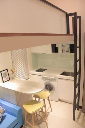 A compact kitchen with a washing machine, a dining area with a table and two chairs, and a blue sofa. - Ha Ha Cat Home Shipai (Taipei)