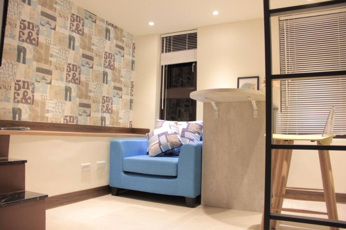 A corner room with a blue sofa, a patterned wall, a window with blinds, and a wooden ladder.