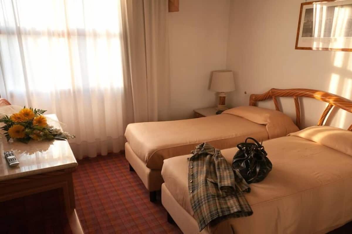 A hotel room with two beds, a desk with a lamp, and a window with curtains.