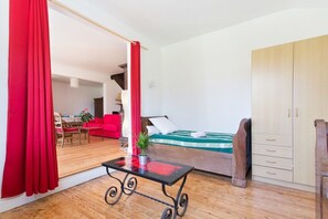 Un dormitorio con cama, armario de madera, cortina roja y una mesita con planta.