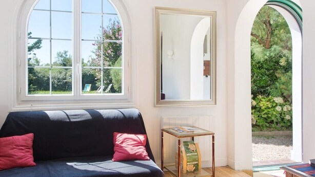A room with a large arched window, a sofa with cushions, a small table with a book, and a mirror on the wall.