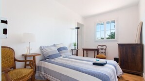 A bedroom with a bed, a chair, a small table, a lamp, and a window.