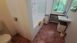 A bathroom with a toilet, a shower, a bathtub, a sink, and a window with a view of greenery. - Apartment 'de Hoamat' with Mountain View & Terrace (Bischofswiesen)