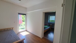 Una habitación con una cama, una puerta que da a un balcón y una ventana con persianas.