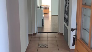 Un pasillo con piso de baldosas, una puerta de madera y vista a una habitación con cama y ventana.