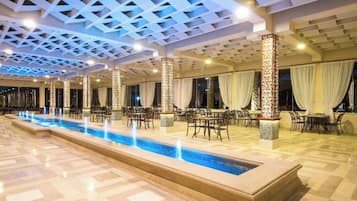 Eine Hotelhalle mit einem langen Pool, Sitzbereichen und dekorativen Säulen.