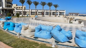 A hotel courtyard with outdoor seating, palm trees, and a pool area. - One bedroom "Beach Haven" in 5-stars resort with pool and private beach (Sahl Hasheesh)