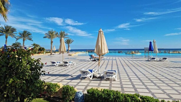 A beachside resort with sun loungers and umbrellas, a pool, and palm trees. - One bedroom "Beach Haven" in 5-stars resort with pool and private beach (Sahl Hasheesh)