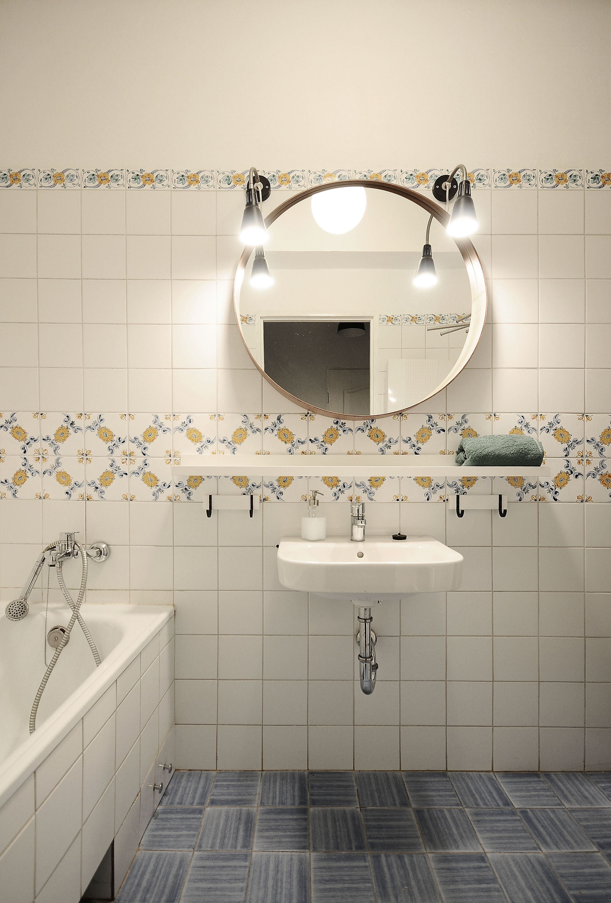 Un baño con un lavamanos blanco, un espejo con iluminación, una bañera y baldosas con diseño.