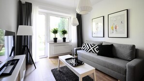 Ein modernes Wohnzimmer mit grauem Sofa, einem weißen Couchtisch, einer Stehlampe und einem großen Fenster mit Vorhängen.