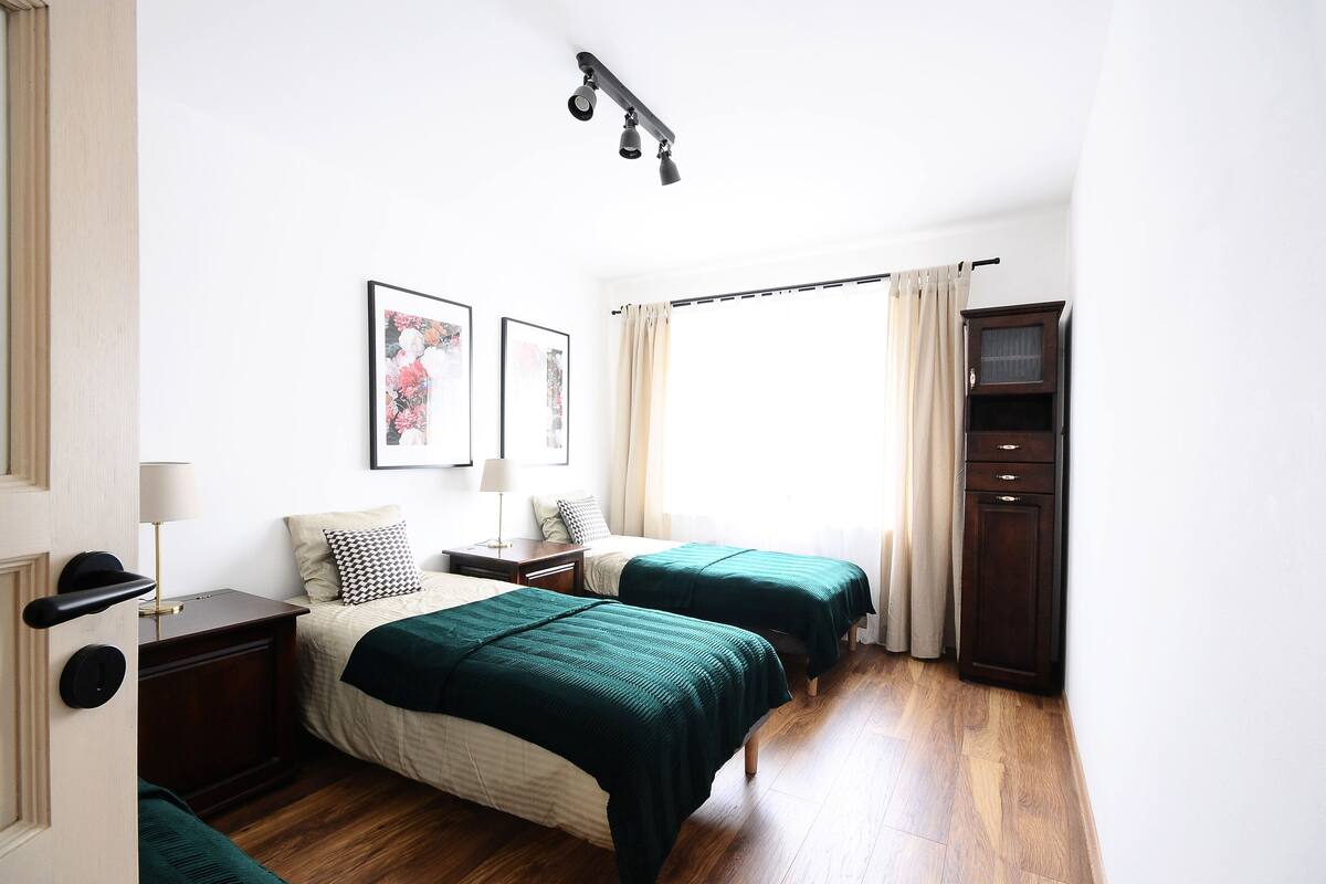 Een slaapkamer met twee bedden, een houten vloer, een kledingkast en een raam met gordijnen.