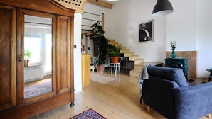 Ein geräumiges Wohnzimmer mit Holzboden, einem dunkelblauen Sofa, einer Treppe und einem grünen Herd.