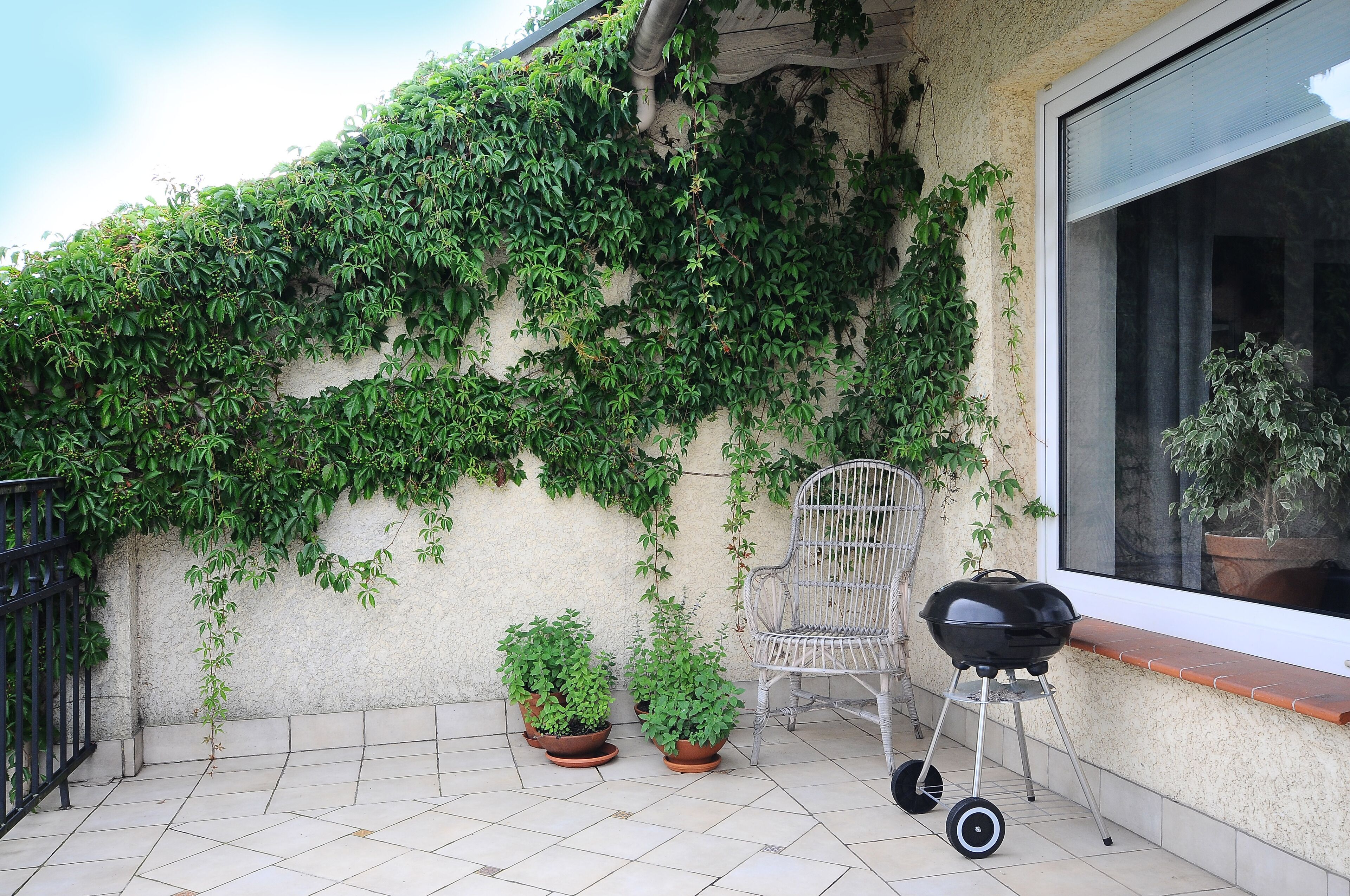 A balcony with potted plants, a grill, and a chair.