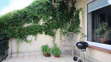A balcony with potted plants, a grill, and a chair.