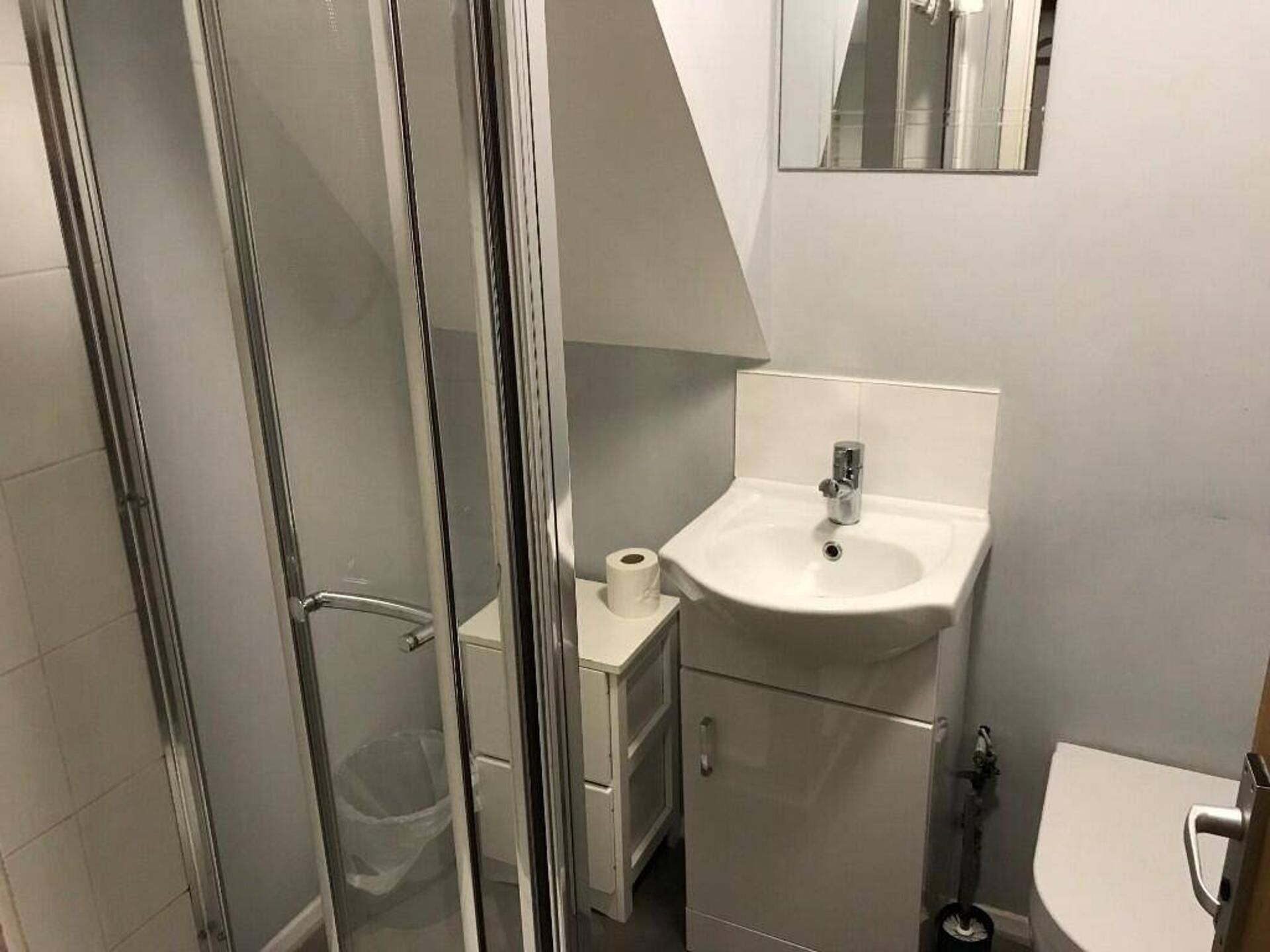 A bathroom with a glass shower enclosure, a sink with a mirror, and a toilet.