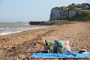 A beach with a picnic setup including a basket, bottles, and a blanket. - Coastal Chalet - Sleeps 6 - Pool - Parking (Deal)