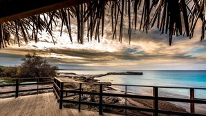 A wooden deck with a railing overlooking a beach with rocky terrain and a body of water. - Baia Verde Concy's Apartment Gallipoli (Gallipoli)