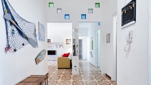 A hallway with patterned floor tiles, a bed with a red pillow, and a net with paddles on the wall. - Baia Verde Concy's Apartment Gallipoli (Gallipoli)