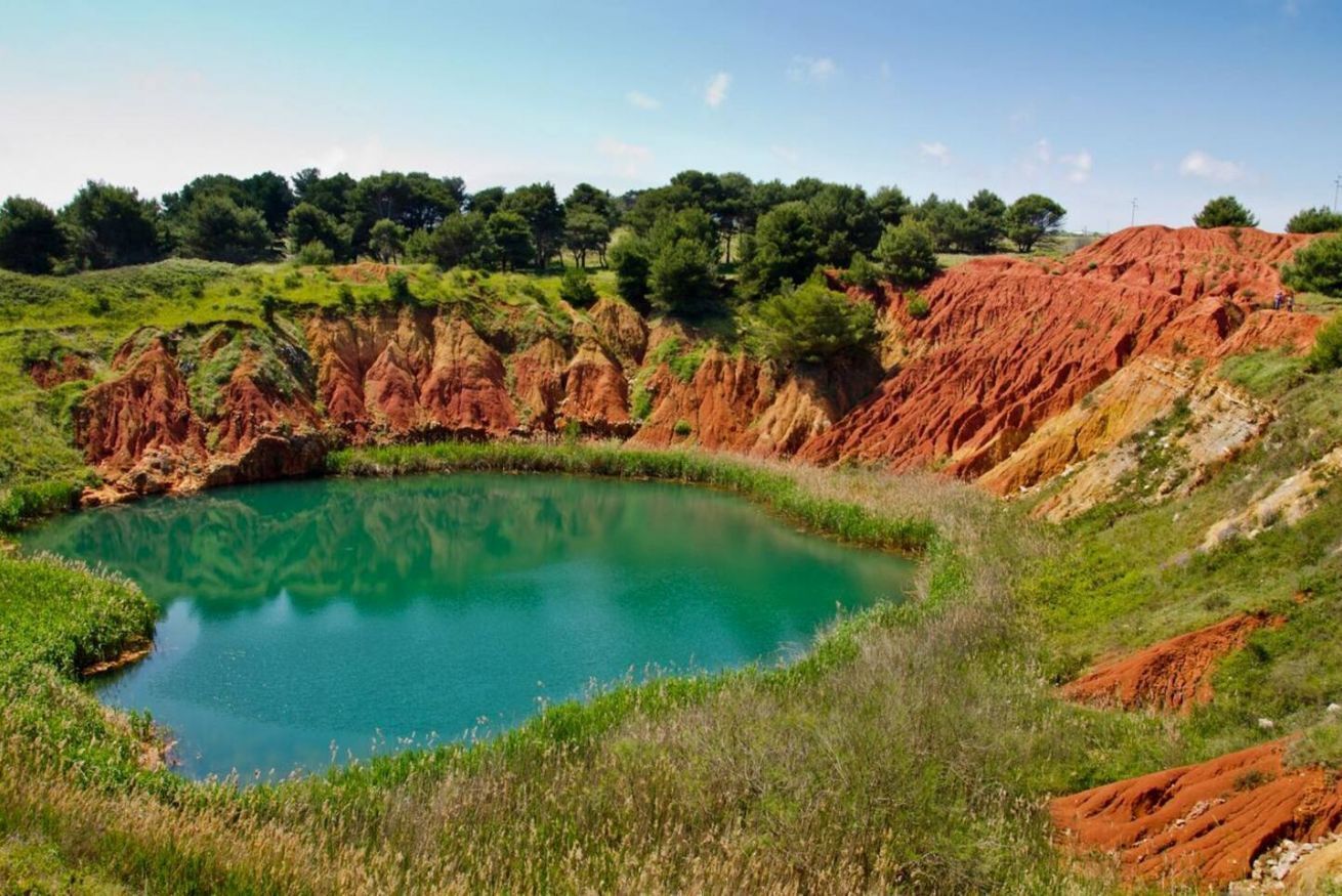 A natural landscape with a pond surrounded by red and green hills.