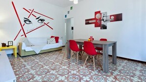 A modern living room with a sofa, dining table, and chairs. There are abstract wall art pieces and a patterned floor. - Baia Verde Concy's Apartment Gallipoli (Gallipoli)
