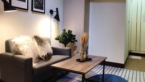 A modern living room with a sofa, a coffee table, and a floor lamp. There are framed pictures on the wall and an air conditioning unit above. - Ha Ha Cat Home Ximending (Taipei)