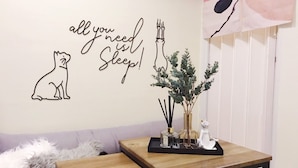A room with a wall decoration featuring a cat, a candelabra, and a quote saying 'all you need is sleep!'. There is a small table with a vase of greenery and a decorative item on it. - Ha Ha Cat Home Ximending (Taipei)